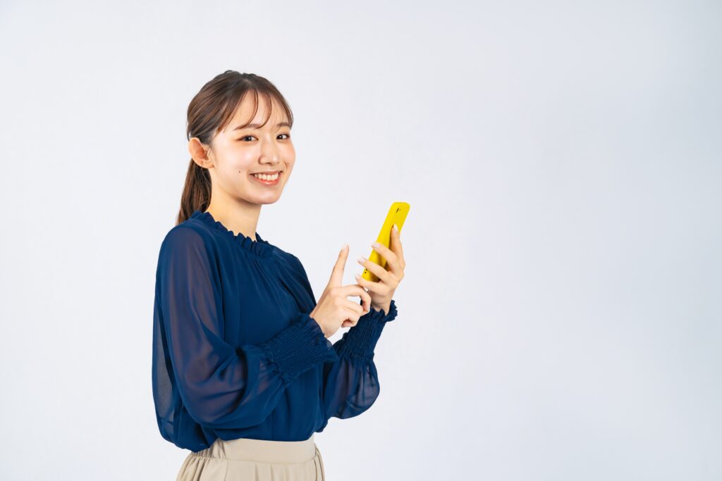 女性がスマホを持ってこちらを笑顔で見ている様子